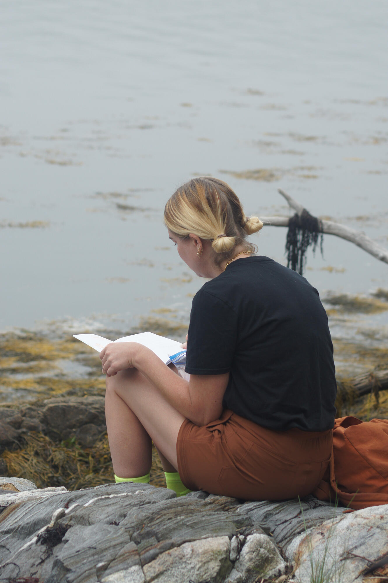 A camper, sitting on the shore, writing in a Nature Journal
